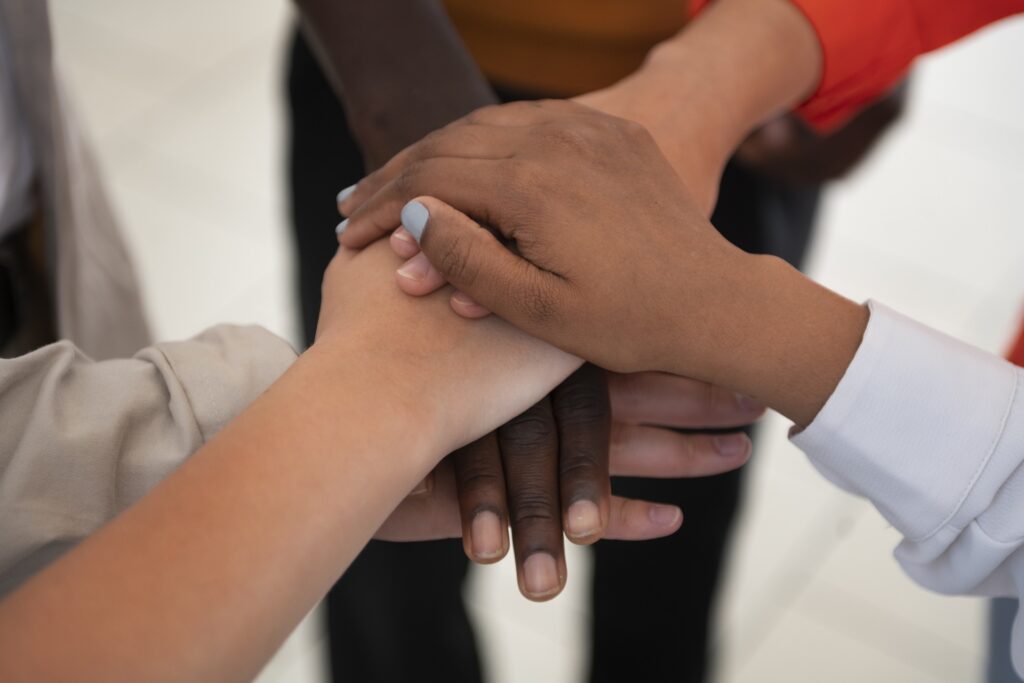 cinco mãos de pessoas diferentes, uma mão sob a outra, as pessoas são de raças diferentes